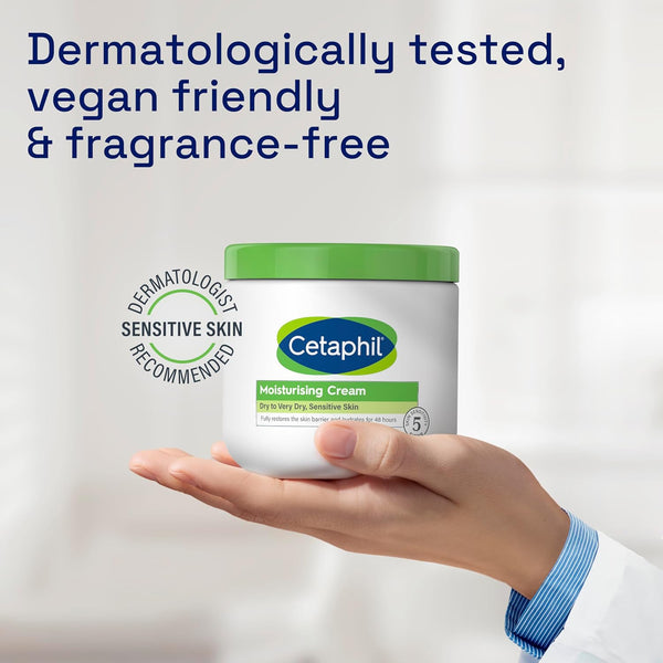 A hand holds a 450g jar of Cetaphil Moisturising Cream with a green lid against a soft background. Text states, Dermatologically tested, vegan friendly & fragrance-free. Labels highlight its 48-hour hydration for dry sensitive skin and dermatologist recommended formula.