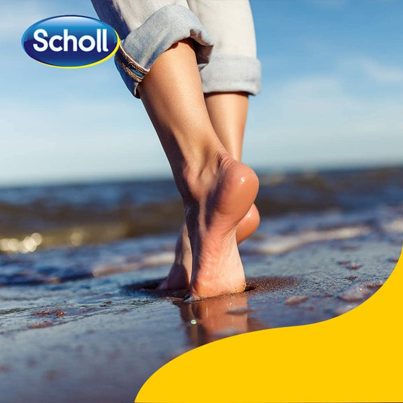 Bare feet stroll on wet sand by the sea, jeans rolled up and reflected in the water. The Scholl logo sits top left, with a yellow wave at bottom right—evoking the freshness and odour protection of Scholl Fresh Step Anti-Perspirant Foot Spray (150ml).