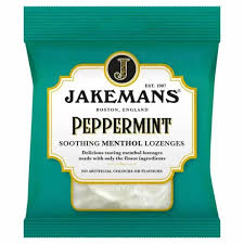 The green packet of Jakemans Peppermint Soothing Menthol Lozenges features gold and white text, highlighting the brand’s 1907 establishment and natural ingredients. Enjoy their refreshing taste through a clear window showcasing these soothing lozenges.