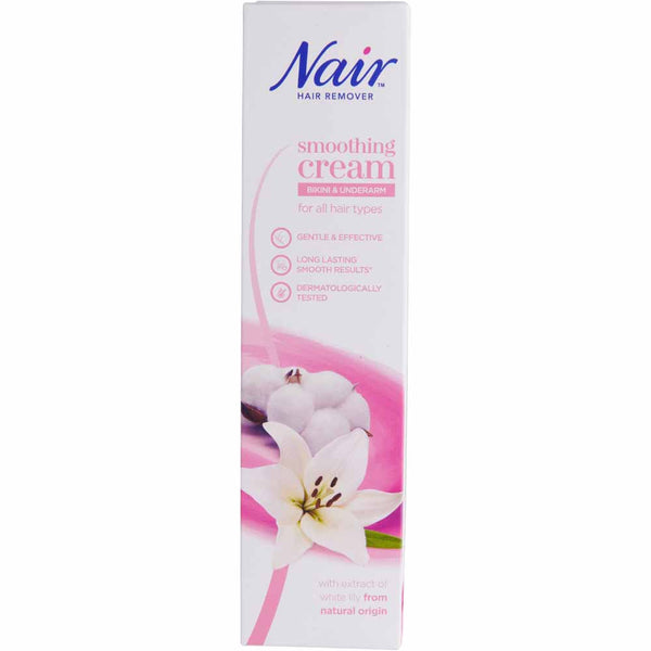 Front of a Nair Smoothing Cream for Bikini and Underarm (100ml) box by Nair, in pink and white, with a white lily flower and smooth stones. Features natural lily extract for gentle, moisturising hair removal on all hair types.