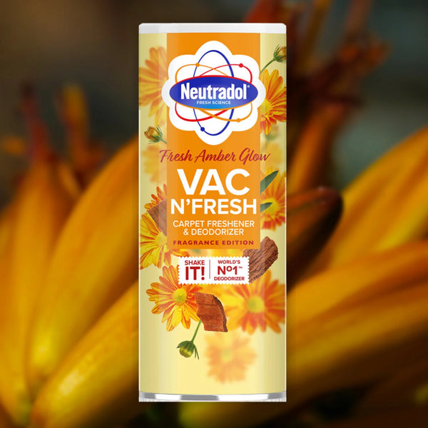 A 350g container of Neutradol Vac Scents Fresh Amber Glow Carpet Deodorizer, decorated with yellow and orange flowers and a cinnamon stick, set against a blurred floral background.