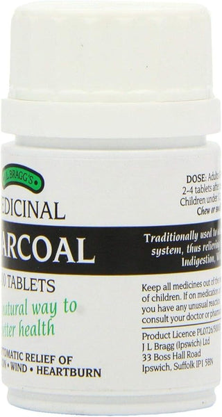 A white bottle of Braggs Charcoal (100 Tablets), sourced from sustainable coconut shells, is labeled for indigestion, wind, and heartburn relief. Dosage instructions and manufacturer details from J L Bragg (Ipswich) Ltd are featured.