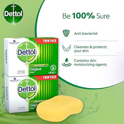 Two boxes of Dettol Original Soap Twin Pack (2 x 100g) and a yellow bar are set against a green splash background, highlighting: Be 100% Sure, Anti-bacterial, Cleanses & protects your skin, and Contains skin moisturizing agents.