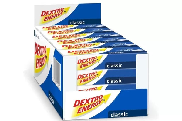 The Dextro Energy Tablets - Classic (24 pack) by Dextro Energy provide a quick energy boost. The display box features a yellow and red logo on a white background with blue accents, perfect for those in need of a quick pick-me-up.