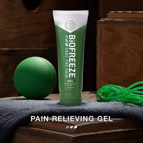 A tube of Biofreeze Pain Relieving Gel (118ml), celebrated for its cryotherapy benefits, rests on a wooden shelf next to a green massage ball and resistance band. A dark gray towel is beside it. The text reads Pain Relieving Gel.