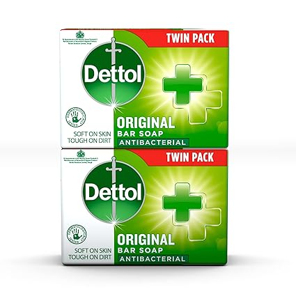 The image shows a Dettol Original Soap Twin Pack (2 x 100g) with green and white packaging featuring a cross symbol. It claims to be soft on skin, tough on dirt, providing a moisturizing experience with antibacterial protection.