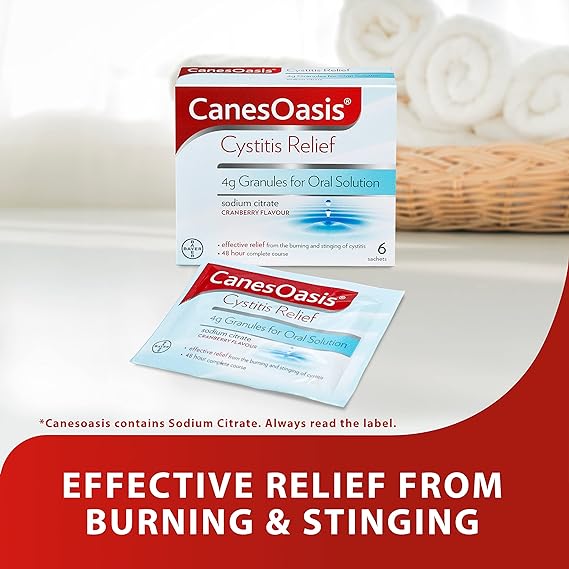 The CanesOasis Cystitis Relief Oral Solution features a box with cranberry-flavored sachets, providing effective relief from burning and stinging sensations. A basket with towels is elegantly displayed in the background.