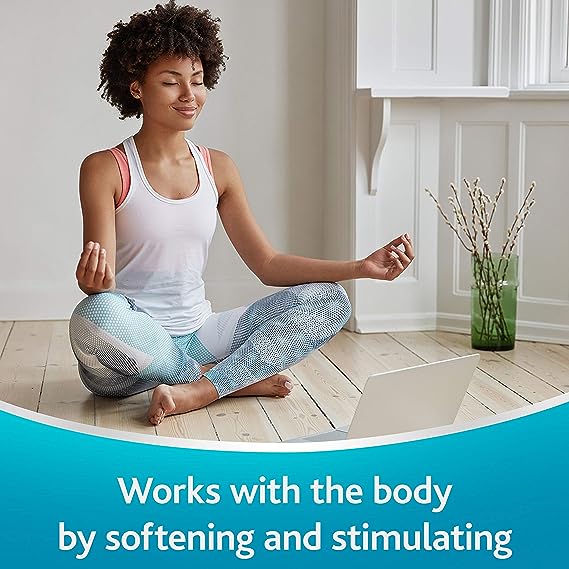 A woman in a white tank top and blue leggings meditates cross-legged on a wooden floor near a laptop. The text reads, Works with the body by softening and stimulating, much like DulcoEase 100mg (30 Soft Gel Caps) from Dulcoease for constipation relief.