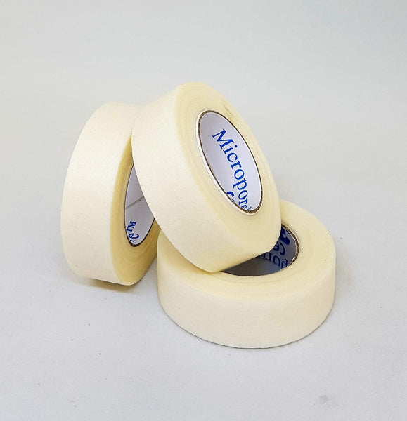 A pack of three MICROPORE Micropore Surgical Tapes (5m x 1.25cm) is stacked pyramid-style on a gray surface, with the top roll tilted to partially show its inner label, known for its gentle adhesive ideal for sensitive skin.