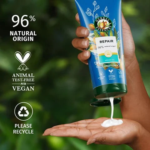 A hand dispenses white lotion from a 250ml bottle of Herbal Essences Conditioner Argan Oil onto another hand. Text notes its 96% natural origin, animal test-free, vegan, and recyclable, with icons for each benefit.