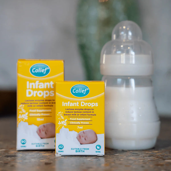 Two boxes of Colief Infant Drops (15ml) by Colief, effective for colic relief with lactase enzyme, are on a countertop next to a milk-filled baby bottle. The yellow boxes feature the blue Colief logo, emphasizing suitability from birth and milks lactose content reduction.