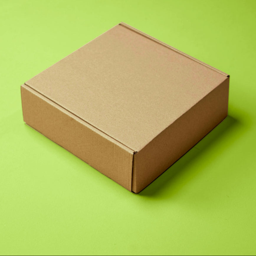 A closed, brown cardboard box sits on a bright green background. The box is placed slightly to the right, leaving a large area of the green surface visible on the left.