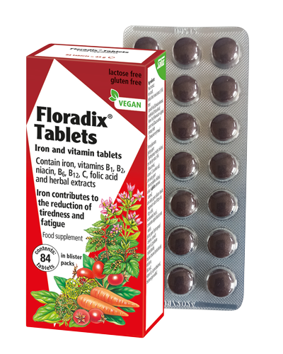 A box of Floradix Iron & Vitamins Supplement (84 Tablets) displays vegan and allergen-free icons with fruit and vegetable images, enhancing blood formation. A blister pack beside it contains brown tablets enriched with Vitamins C and B-group.