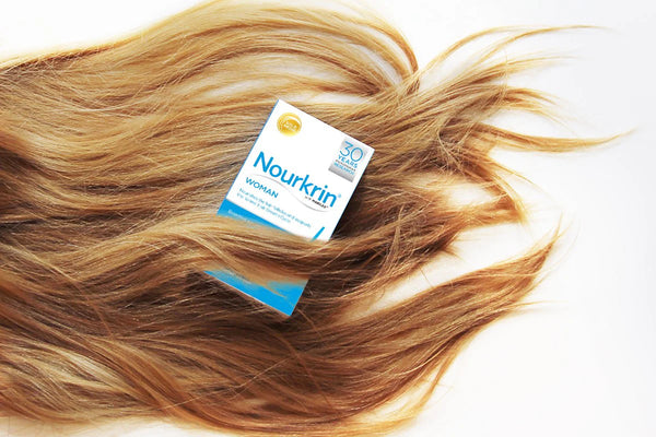 A box of Nourkrin Woman (60 Tablet) by Nourkrin sits on light brown hair spread over a white background, supporting healthy hair growth with marine proteins.