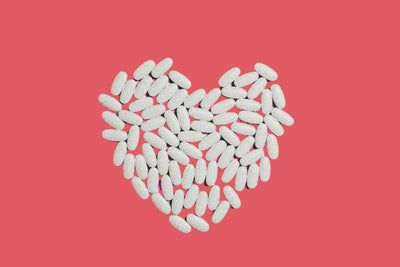 White pills arranged in the shape of a heart against a red background.